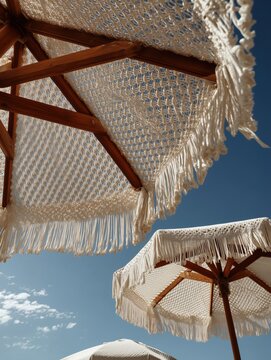 Three handmade macrame beach umbrellas with tassels and wooden frames captured from a low angle looking up into the cloudless sky.