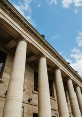 beige columns of a classical building exterior against a partly cloudy blue sky
