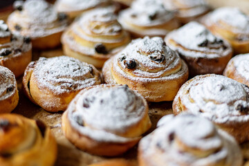 Close-up of freshly baked pastries topped with powdered sugar and raisins, emphasizing texture and...