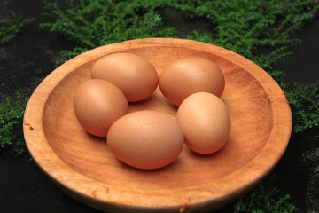 Top view of chicken eggs on a wooden plate with green grass surrounding them in the background