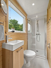 Compact modern tiny house bathroom with wood paneling, glass shower and window – minimalist interior with smart space-saving layout and natural light