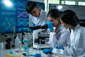 Three young scientists in lab coats working together in a laboratory examining a petri dish for...