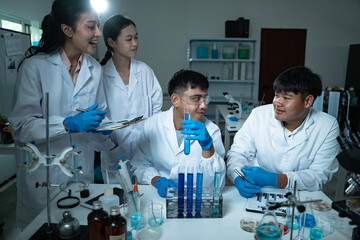 In the laboratory, a group of professional researchers gather around a chemical tube, checking...