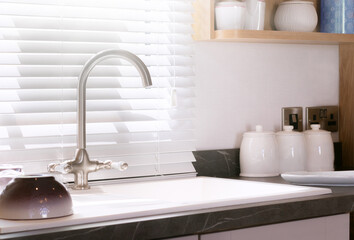 Kitchen interior featuring kitchen sink and marble counter with built it overmount basin inset with brushed nickel faucet. Traditional feel with white window blinds.
