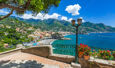 Coastal town panorama. Cliffside buildings overlook a beach and blue ocean under a clear sky with greenery