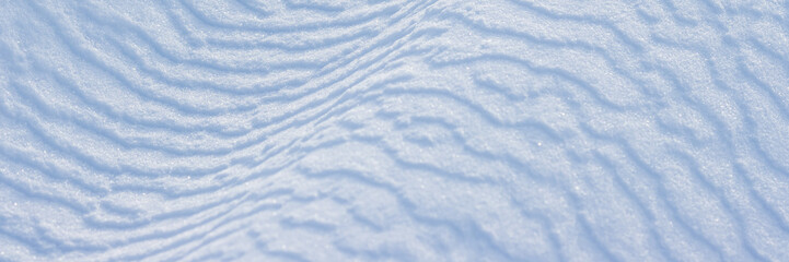Beautiful winter background with snowy ground. Natural snow texture. Wind sculpted patterns on snow surface. Wide panoramic texture for background and design.