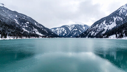 Obraz premium tranquil teal lake surrounded by majestic snow capped mountains creates serene winter landscape. calm water reflects beauty of nature, inviting peace and contemplation
