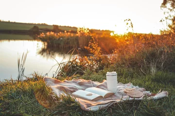 Fotobehang Herfst Bible on plaid blanket with coffee cup and autumn leaves near peaceful riverbank at sunset. Tranquil outdoor scene of spiritual reflection, nature, and calm during golden hour  © shine.graphics