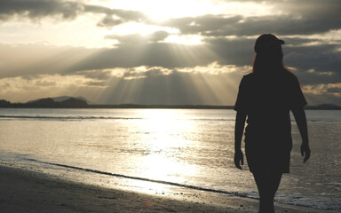 Fototapeta premium Silhouette of a woman with hat standing on the beach in the morning