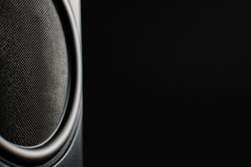 Close-up view of a sleek black speaker with a matte finish showcasing a prominent woofer, elegantly lit to highlight its modern design and minimalism