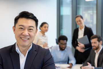 Fototapeta premium An asian businessman smiles confidently for the camera in front of his team during a meeting at the office.