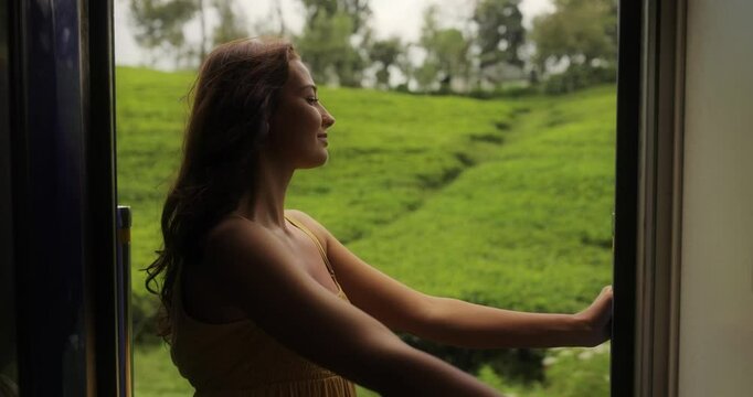 Travel and exploration of tourist woman by Sri Lankan train in second class wagon to famous places of the country. Romantic young traveler woman enjoying extreme train ride, looking out to the door on