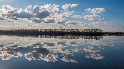 Obraz premium Magic symmetrical reflection of clouds in water. Spring landscape with river an far forest. 