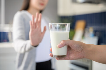 Allergy dairy food lactose intolerance allergen health care illness concept. Selective focus on a glass of milk with blurred woman gesturing refusing stop or reject say no to cow milk.