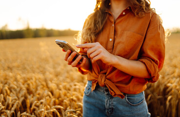Beautiful female farmer standing in golden wheat field with phone. Female agronomist with phone and...