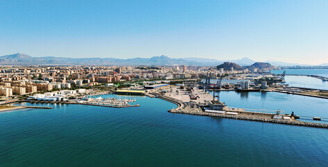 Aerial view of marina filled with numerous docked boats in the clear turquoise water of Mediterranean Sea and urban landscape of Alicante town, Spain. Costa Blanca