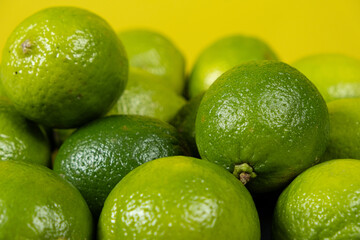 Whole fresh limes fruit on yellow background close-up.
