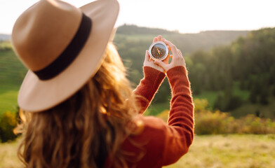 A beautiful woman in a hat and holding a compass stands on a green hill with a stunning view. Young...