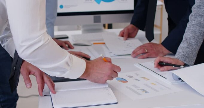 Close up shot of a coworkers working together on business research during an office meeting. They are handling documents and using a computer, focusing on accounting tasks to achieve goals.