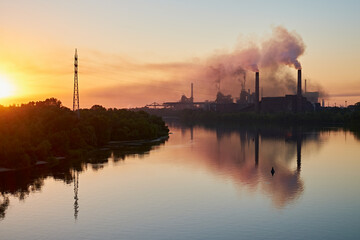 Industrial plant with smoking chimneys at sunrise, reflecting in a calm river. Dniprovskyi Coke...