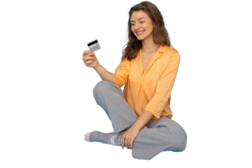 Smiling young woman holding a credit card while sitting with crossed legs on a transparent background