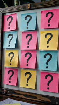 Vibrant sticky notes with handwritten question marks scattered across blank whiteboard, depicting collaborative problem solving workspace.
