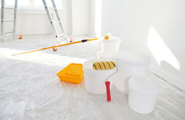 Close up of buckets with paint rollers standing in empty new house with freshly painted white walls...