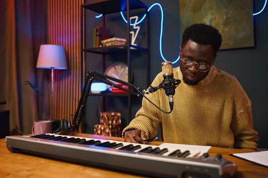 African American man sitting at table with synthesizer and microphone and reading content plan before podcast