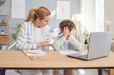 Caring mother providing support and assistance to sad, crying schoolboy son with homework during online learning at home. Family support in education, especially during challenging times.