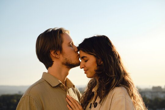 Young man gently kisses woman on the forehead during golden hour. A serene and emotional moment of love, intimacy, and trust between a couple in natural outdoor light.