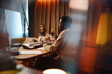 Young African American woman singing in microphone with man playing melody on synthesizer during...