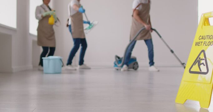 Team of professional cleaners or service workers washing office room, mopping and vacuuming floor, dancing carefree and having fun, almost finishing doing cleaning up, performing their duties