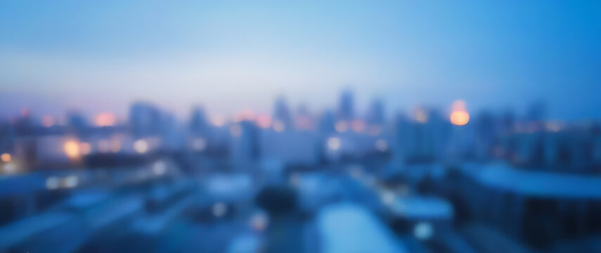Blurred cityscape with buildings and lights at dusk or dawn in blue tones.