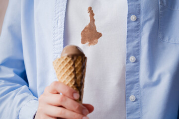 A person holding chocolate ice cream cone, spilled ice cream on white clothes. Concept of daily...