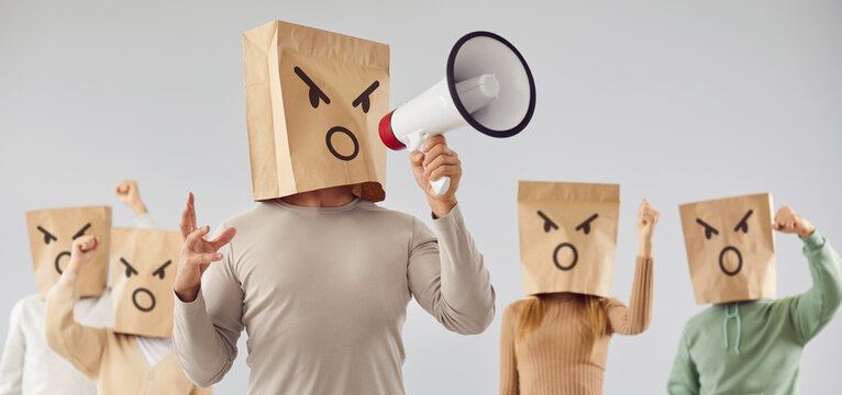 Faceless anonymous male person leader wearing paper bag mask on head shouting in megaphone making announcement with angry crowd of people behind. Leadership and unity concept. Banner.
