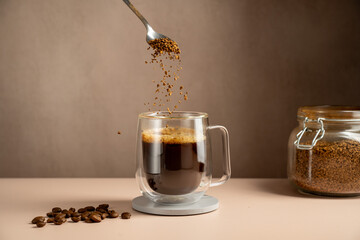 Instant coffee pouring in transparent glass mug, roasted coffee beans