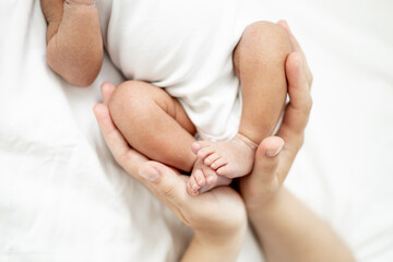 mom's hands of a white-skinned woman gently stroke the tummy or massage a newborn African-American baby, a small child lies on the bed in the bedroom after waking up or falling asleep