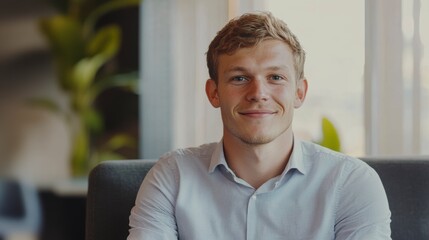 Naklejka premium Happy young man smiling, seated in a comfortable chair indoors.