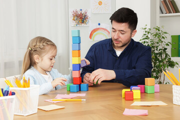 Teacher and little girl with colorful cubes at desk indoors