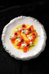 Vibrant dish featuring thinly sliced salmon atop a bed of vegetables, adorned with cream and garnishes, elegantly presented on a textured white plate, perfect for fine dining and gourmet showcases.