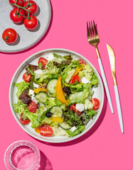 Vegetable salad with lettuce, olives and feta cheese on pink background