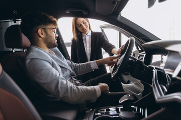 Saleswoman showing steering wheel functions to businessman buying new car