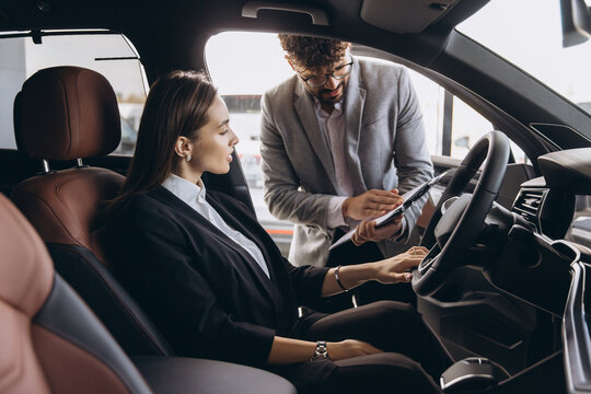 Car salesman showing new vehicle features to businesswoman in car dealership