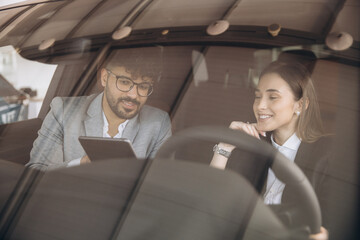 Car salesman showing tablet to customer sitting in new car
