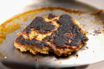 Burnt pancake with black scorched crust on steel pan. Front view