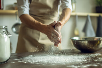 A baker in an apron kneads the dough with his hands and sprinkles it with flour to bake delicious homemade bread.