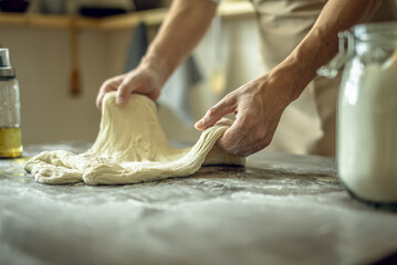 A baker in an apron kneads the dough with his hands and sprinkles it with flour to bake delicious homemade bread.