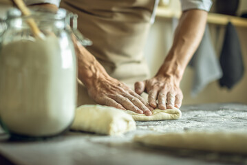 A baker in an apron kneads the dough with his hands and sprinkles it with flour to bake delicious homemade bread.