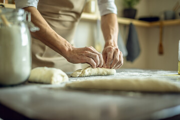 A baker in an apron kneads the dough with his hands and sprinkles it with flour to bake delicious homemade bread.