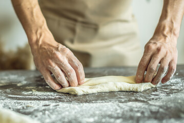 A baker in an apron kneads the dough with his hands and sprinkles it with flour to bake delicious homemade bread.